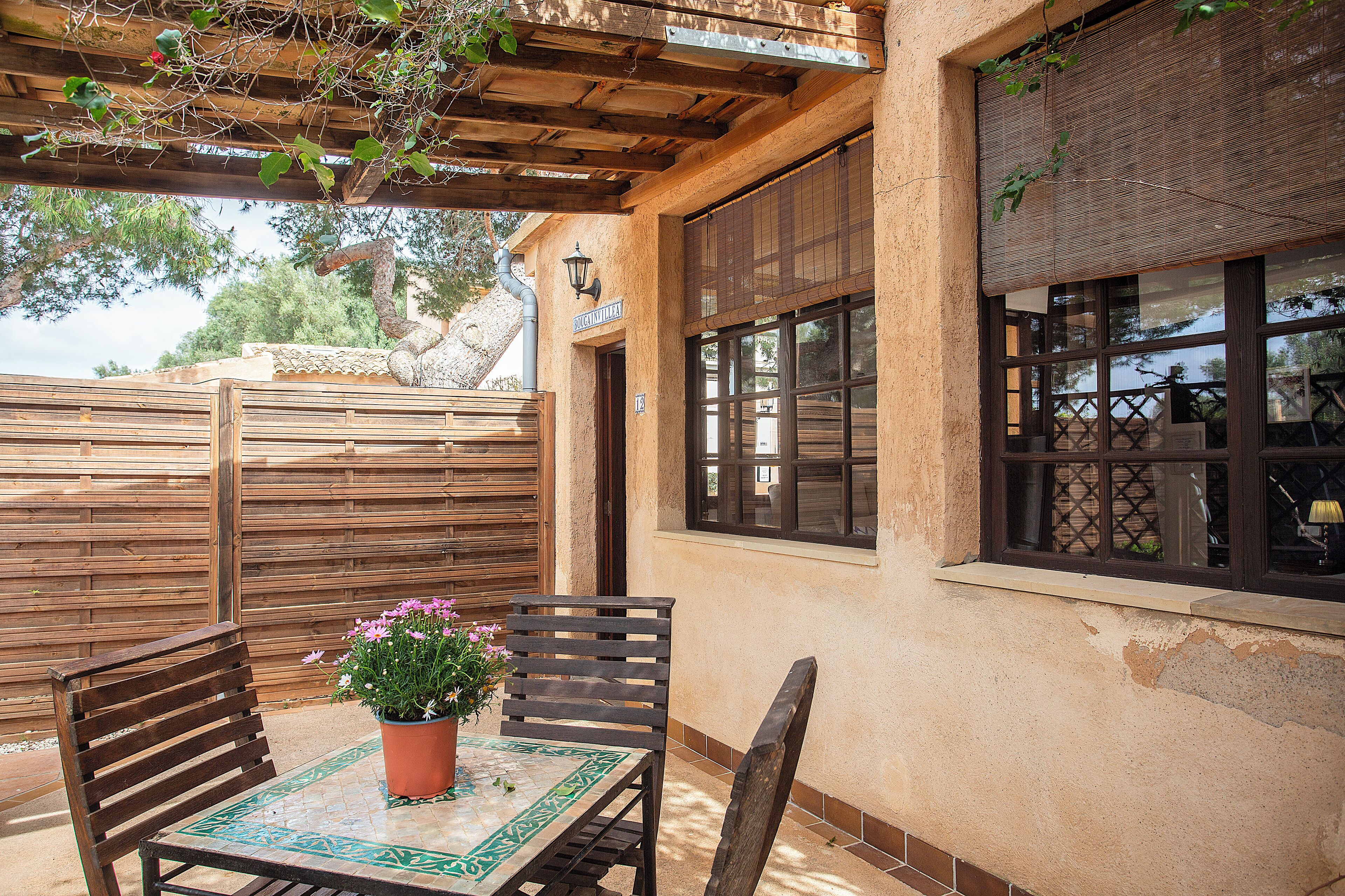 A patio with a wooden table and chairs, a potted plant, and a pergola overhead.