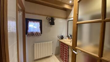 A bathroom with a white radiator, a window with patterned curtains, a sink with a mirror, and a red and white checkered towel.