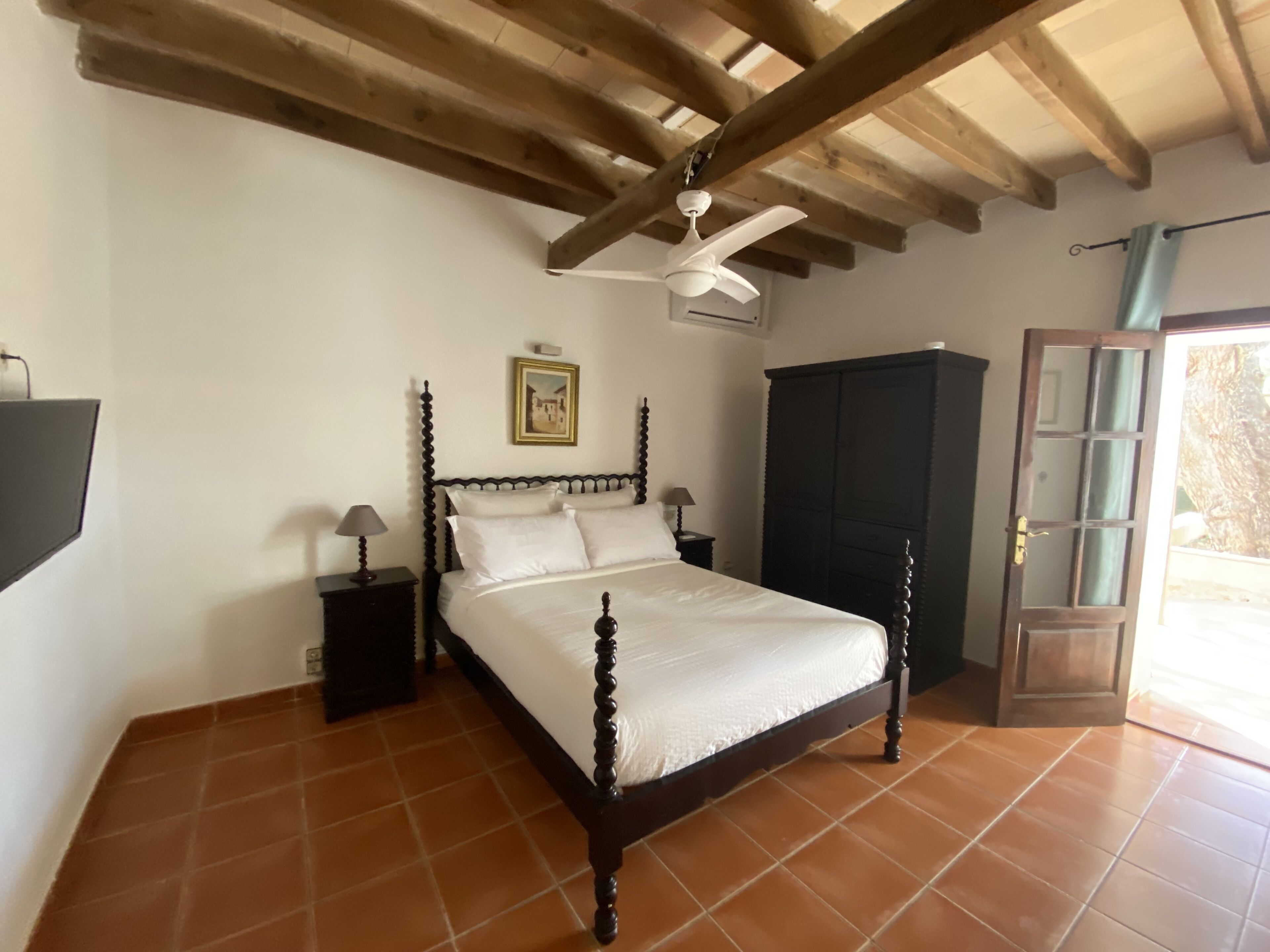 Un dormitorio con cama, mesita de noche, armario y ventilador de techo.