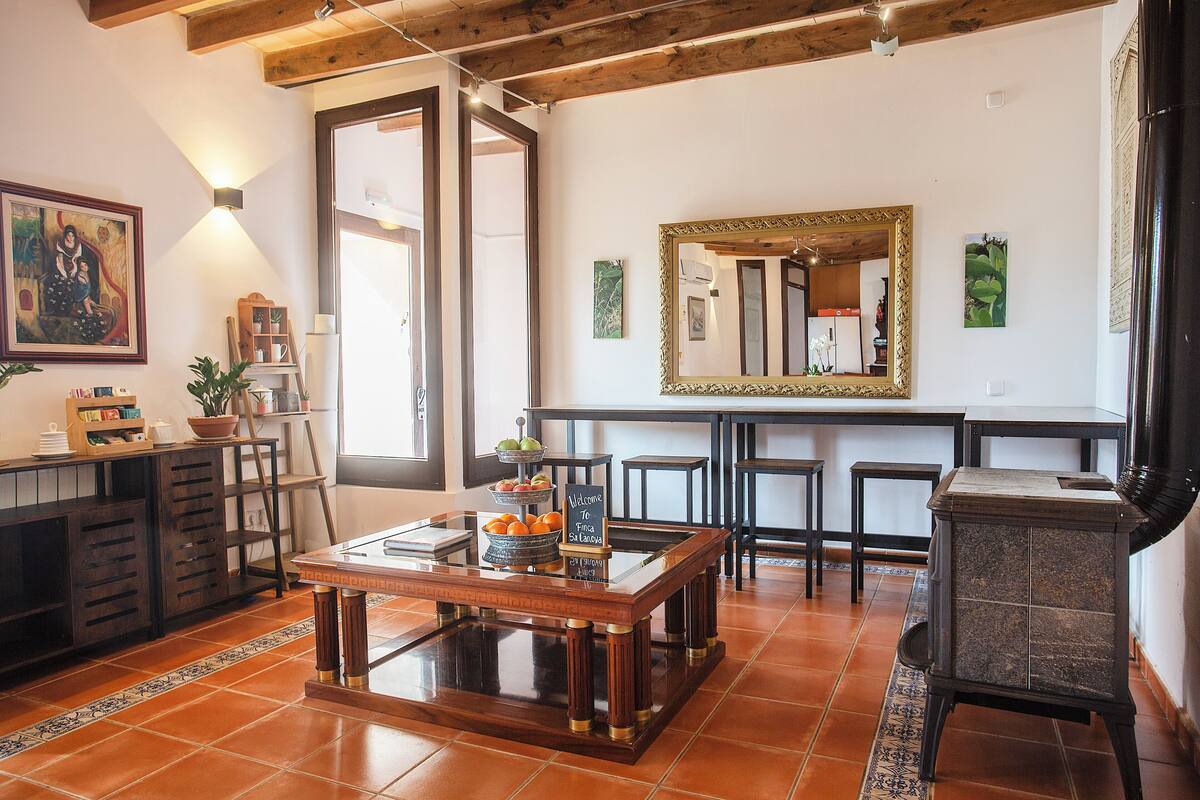 A dining area with a wooden table, chairs, and a buffet setup. There is a large mirror on the wall and a cabinet with drawers.