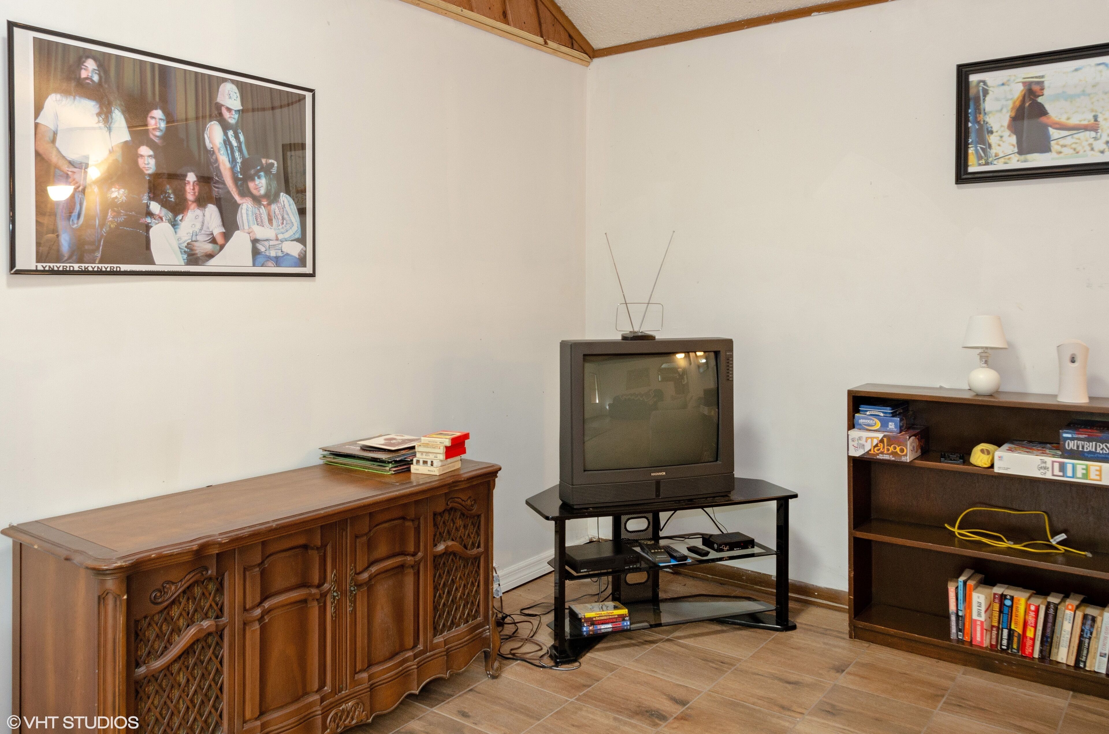 Ett vardagsrum med ett träskåp, en tv på ett stativ och en bokhylla med böcker och dekorativa föremål.