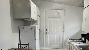 Una cocina compacta con gabinetes blancos, un refrigerador, una estufa y una mesa de comedor con sillas.