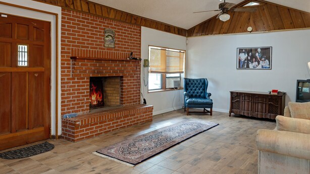 Una sala de estar con chimenea de ladrillo, un sillón azul, un mueble de madera y un ventilador de techo.
