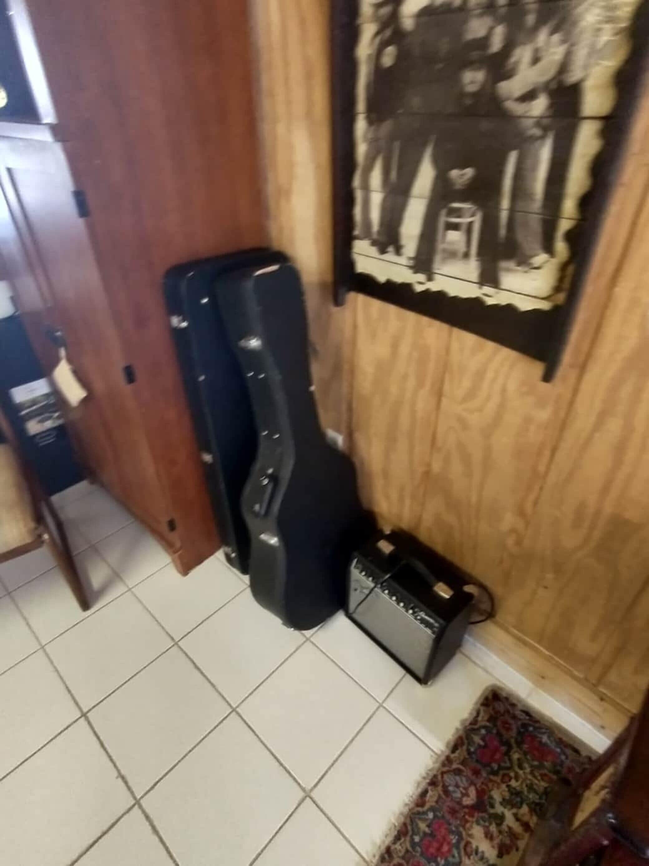 Um quarto com porta de madeira, uma capa de guitarra preta, um amplificador pequeno e um pôster na parede.