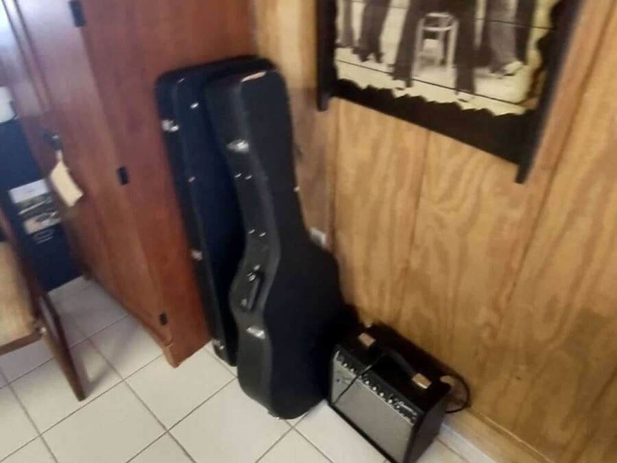 Um quarto com porta de madeira, uma capa de guitarra preta, um amplificador pequeno e um pôster na parede.