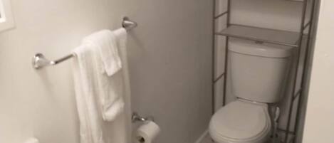 Een compacte badkamer met toilet, wastafel, handdoekhouder en een plank met opgevouwen handdoeken.