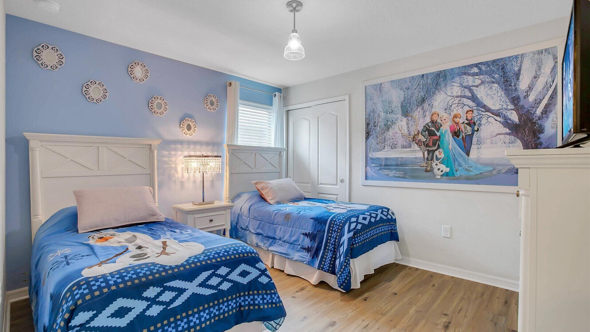 Un dormitorio con dos camas, una araña, un cuadro de un paisaje invernal y placas decorativas en la pared.