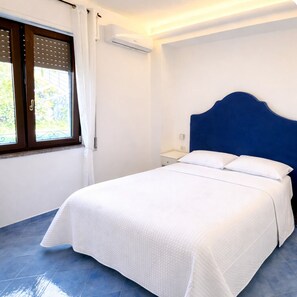 A bedroom with a bed, a window with blinds, an air conditioning unit, and a nightstand. - SEA VIEW APARTMENT with parking  (FURORE)