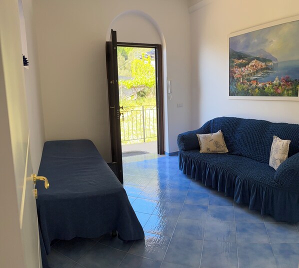 A room with a bed, a sofa, a painting, and a view through an open door.