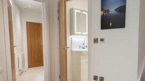 Un pasillo con una puerta de madera, un radiador blanco y un baño con lavabo y espejo.