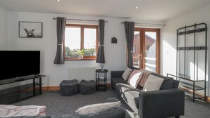 A modern living room with a large flat-screen TV, a sofa, a coffee table, and a window with curtains. - Bluebell Lodge, Meadow View Lodges (Burnham-on-Sea)