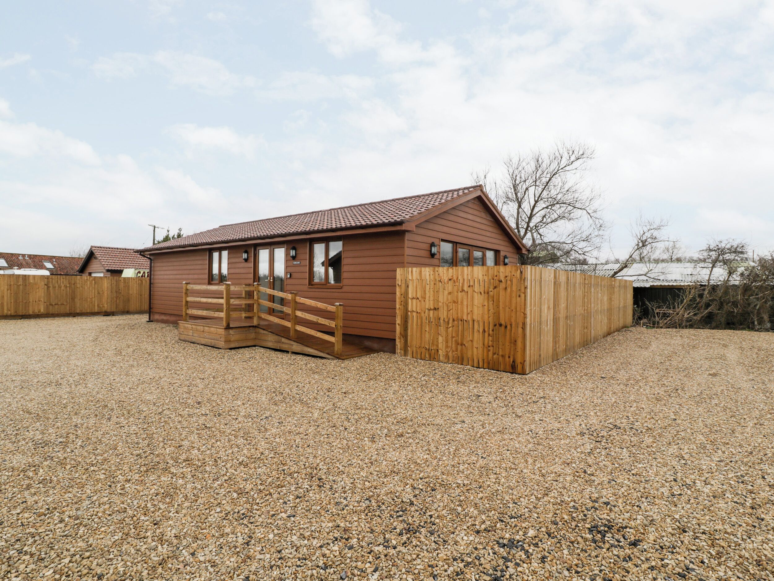 A single-story wooden building with a sloped roof, a wooden gate, and a gravel driveway.