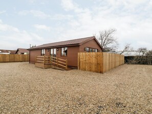 A single-story wooden building with a sloped roof, a wooden gate, and a gravel driveway.