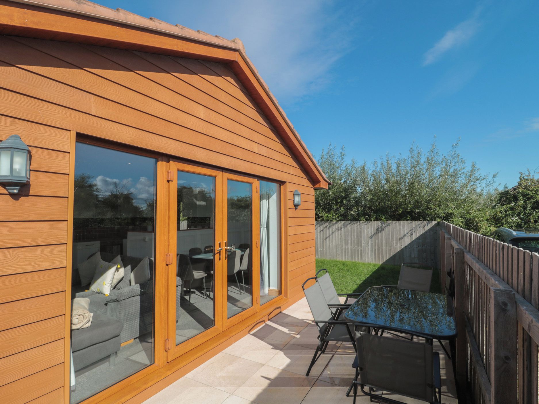 A wooden house with a patio area, including a table and chairs, and a sliding glass door leading to an interior space.