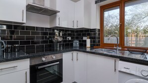 A modern kitchen with black and white tiles, stainless steel appliances, and a built-in washing machine. - Bluebell Lodge, Meadow View Lodges (Burnham-on-Sea)
