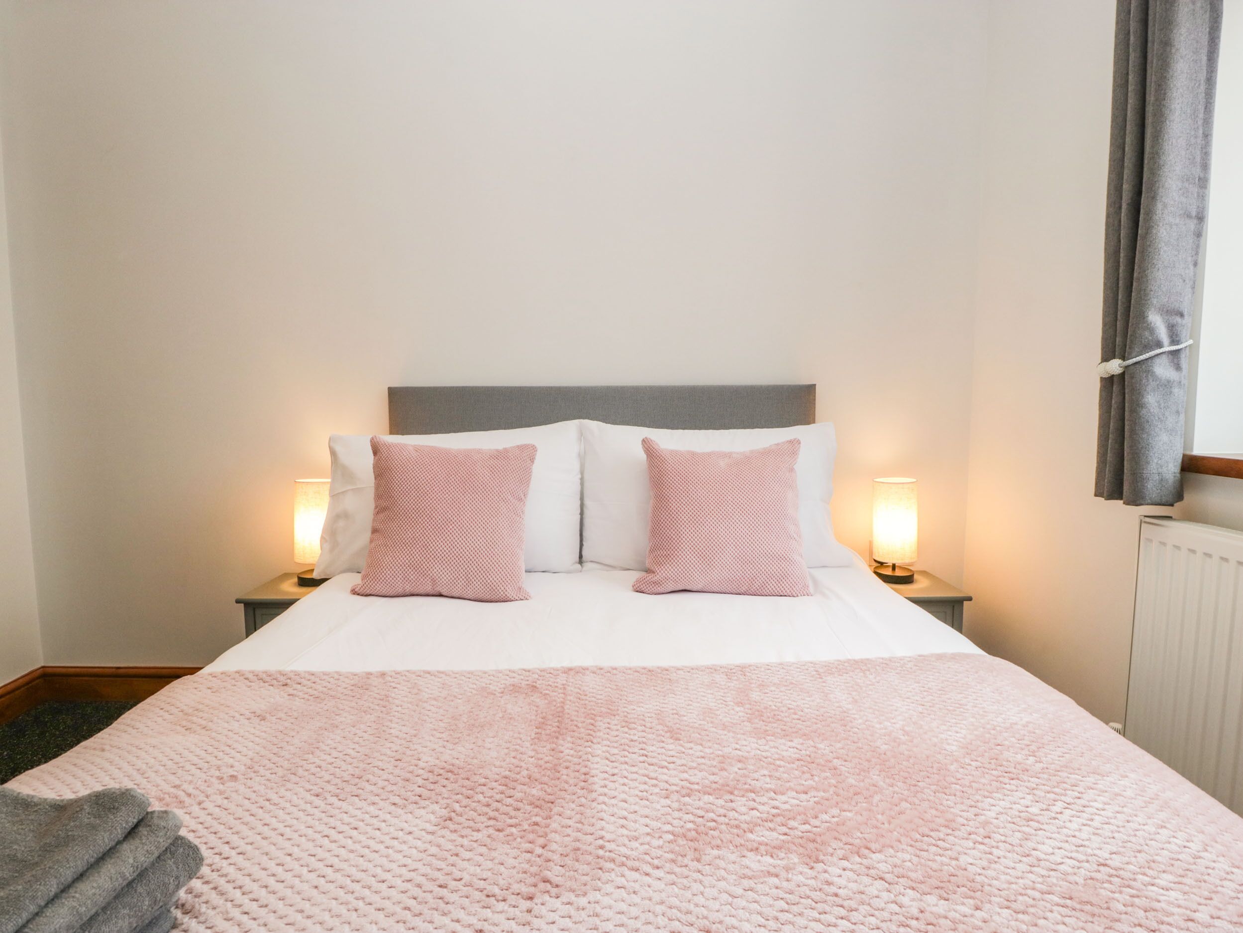 A neatly made bed with a pink blanket, two pillows, and two bedside lamps.