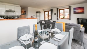 A modern dining area with a glass table set for a meal, a sofa, and a television in the background. - Delphine Lodge, Meadow View Lodges (Burnham-on-Sea)