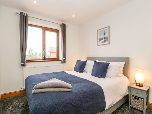 A neatly made bed with a blue and white duvet, a grey headboard, and a bedside lamp.
