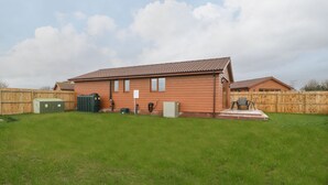 A single-story house with a tiled roof, a fenced backyard, and a small patio area. - Delphine Lodge, Meadow View Lodges (Burnham-on-Sea)