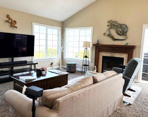 A living room with a sofa, television, fireplace, and large windows.
