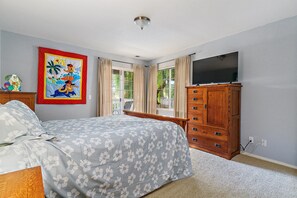 A bedroom with a bed, a wooden dresser, a television, and a window with curtains.