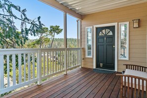 Eine Veranda aus Holz mit weißer Brüstung, einer schwarzen Tür und einer Bank.
