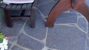 Un patio con un banco y una mesa de madera, rodeado de plantas en macetas y un muro de piedra.