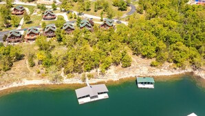 Luchtfoto van een vakantiecomplex aan een meer met meerdere bungalows, een steiger en een boot.