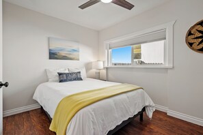 A bedroom with a bed, a window with blinds, a ceiling fan, and a painting on the wall.
