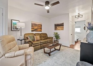 A living room with a sofa, armchair, coffee table, and a ceiling fan.