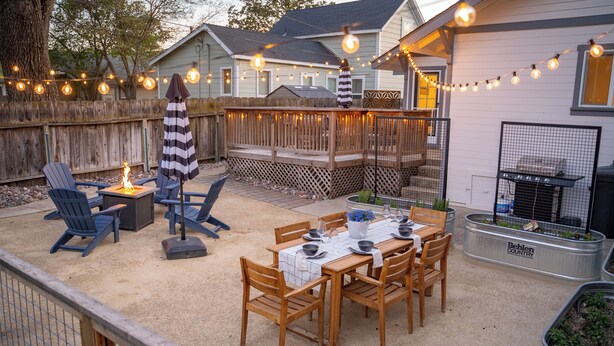 Eine Terrasse im Freien mit Holztisch und -stühlen, einer Feuerstelle und Lichterketten.
