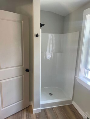 Une petite salle de douche d’angle avec une porte blanche et une fenêtre.