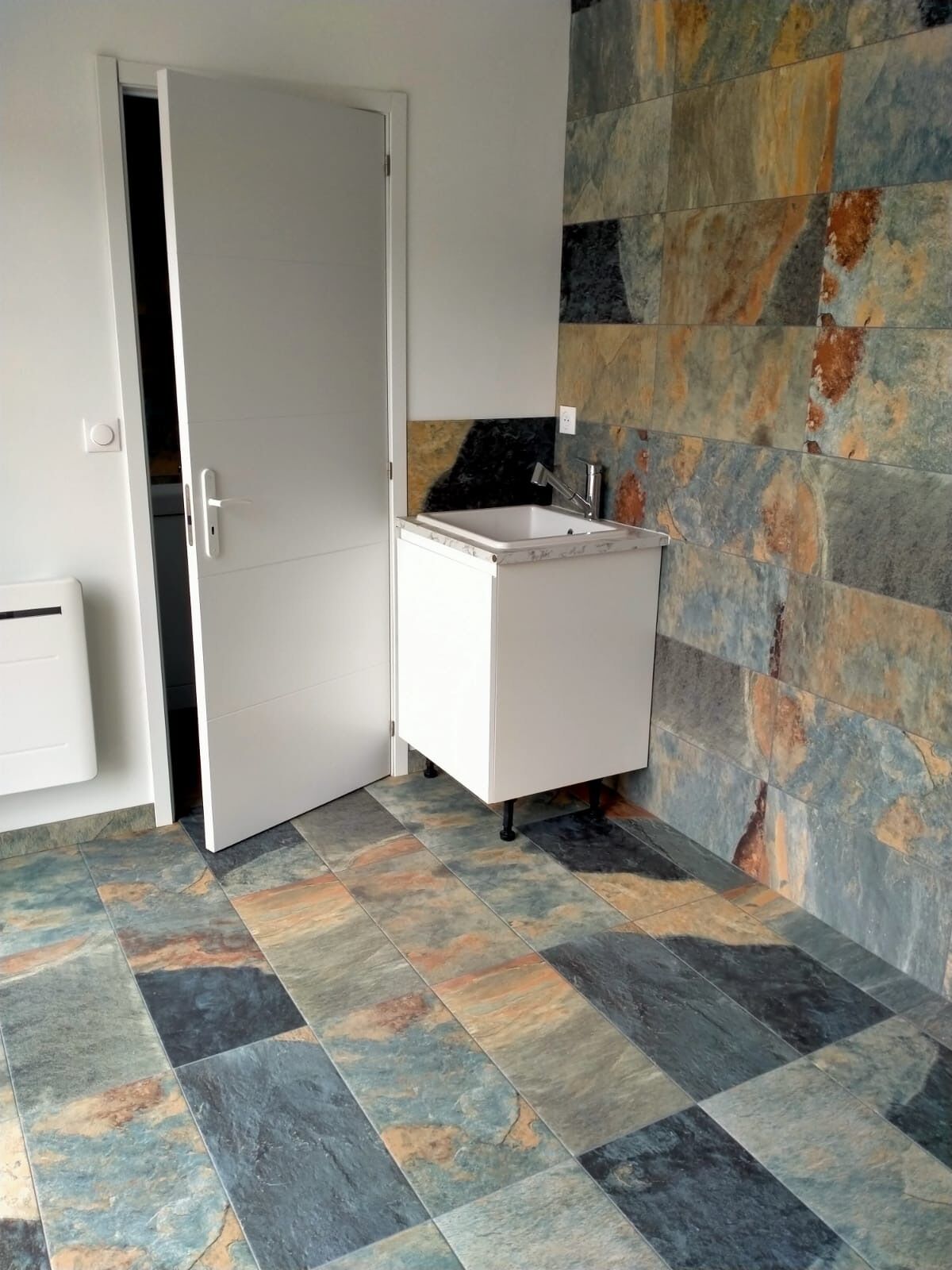 Ein kleines Badezimmer mit einem weißen Waschbecken, einer Tür und Fliesenboden.