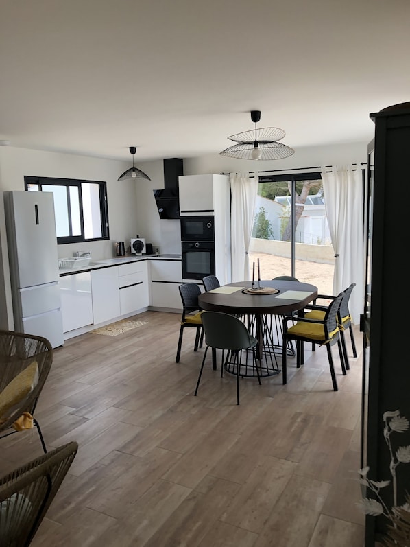 Une cuisine moderne avec des meubles blancs, un four noir et un coin repas comprenant une table ronde et des chaises.