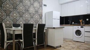 A compact kitchen with a dining area, including a table, chairs, a refrigerator, a washing machine, and a coffee maker. - Beautiful Apartment With Kind And Friendly Owners (tbilisi)