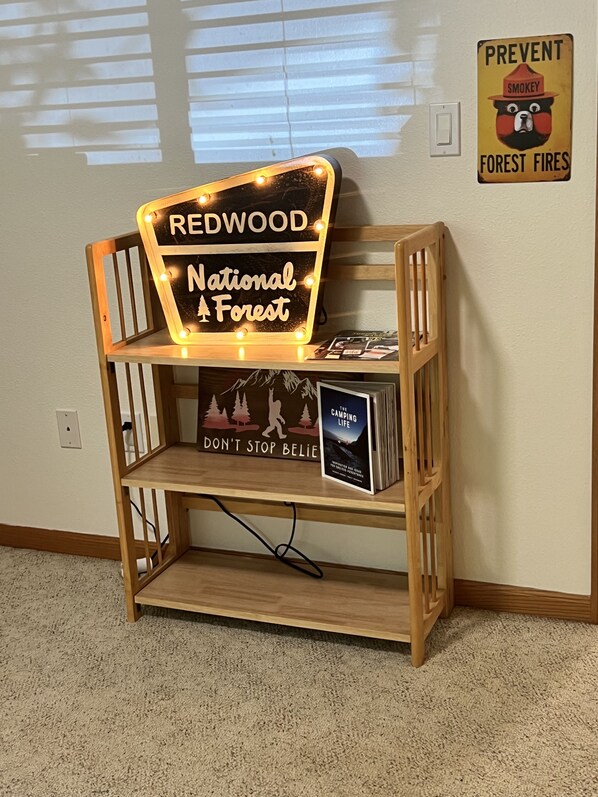 Une étagère en bois sur laquelle est accrochée une pancarte indiquant « Forêt nationale de Redwood » et un livre intitulé « La vie en camping ».