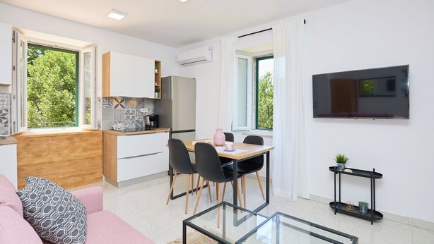 A modern kitchen with a dining area, a sofa, and a TV.