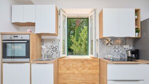 A modern kitchen with a built-in oven, a window with a view of greenery, and a coffee machine.