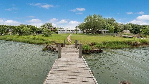 A wooden dock leading to a grassy area with houses in the background. - Lakefront Property with a pool & hot tub! (Groesbeck)