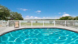 A swimming pool with a white fence, a lounge chair, and a view of a green landscape. - Lakefront Property with a pool & hot tub! (Groesbeck)