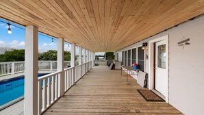 A covered wooden deck with a pool on one side, white railings, and a door with a window. - Lakefront Property with a pool & hot tub! (Groesbeck)