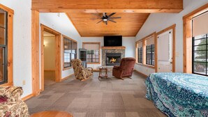 A spacious room with a fireplace, two armchairs, a bed with patterned bedding, and large windows. - Lakefront Property with a pool & hot tub! (Groesbeck)