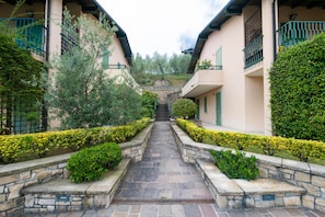 A pathway leading to a building with a stone staircase, surrounded by neatly trimmed hedges and trees. - Apartment Villini del Vittoriale (Gardone Riviera)
