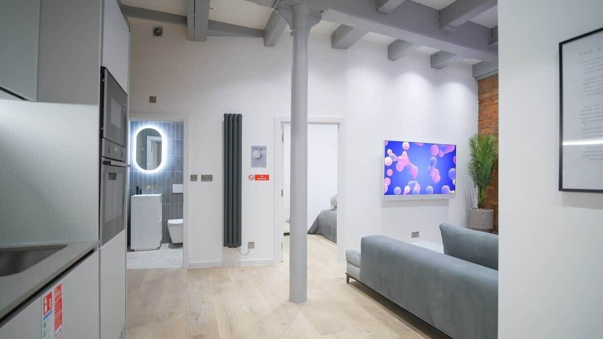 A modern kitchen with a built-in oven, a sink, and a mirror. There is a living area with a sofa and a flat-screen TV.