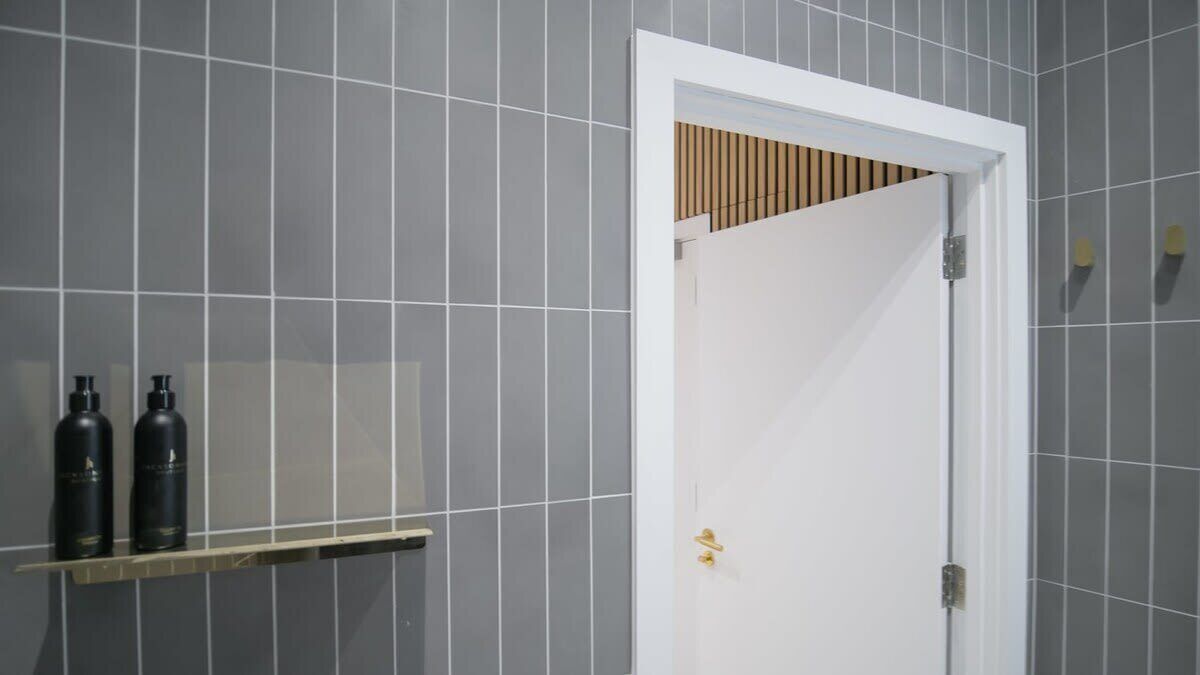 A bathroom with a tiled wall, a white door, and two black bottles on a shelf.