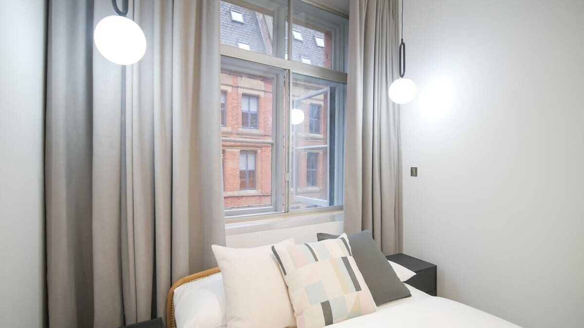 A bedroom with a bed, curtains, a window, and a nightstand.
