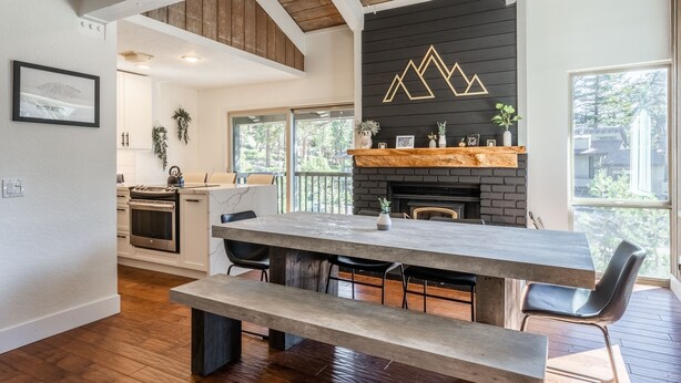 A modern kitchen with a large island, wooden ceiling beams, and a fireplace.