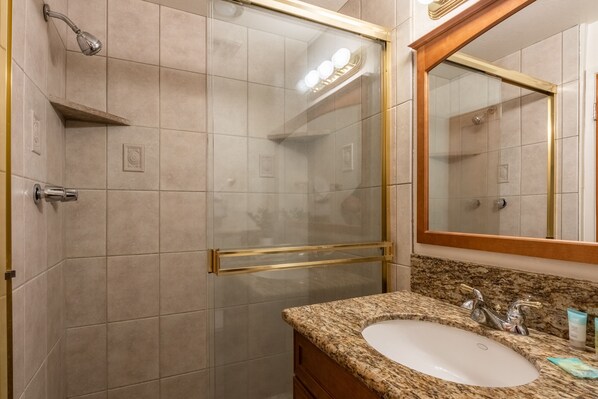 Ein Badezimmer mit einer Duschkabine, einem Waschbecken mit Granitplatte und einem großen Spiegel.
