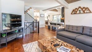 A modern living room with a grey sofa, wooden coffee table, and a TV on a dark wooden stand.