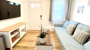 Una sala de estar con un televisor de pantalla plana, un sofá, una mesa de centro con una planta y una estantería.